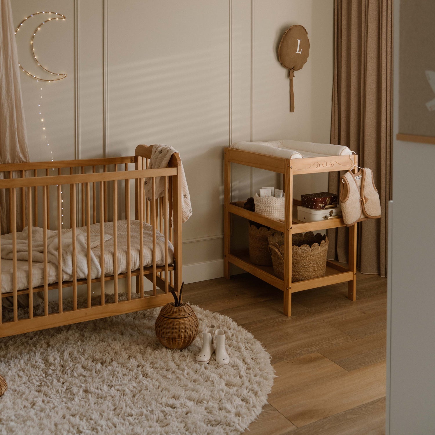 Nursery room with wooden crib and changing table, decorated with string lights and wall hangings.