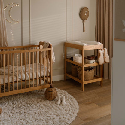 Nursery room with wooden crib and changing table, decorated with string lights and wall hangings.